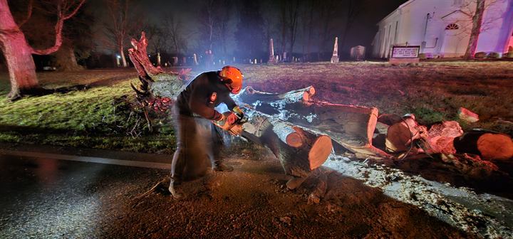 A volunteer cuts through a downed tree at night